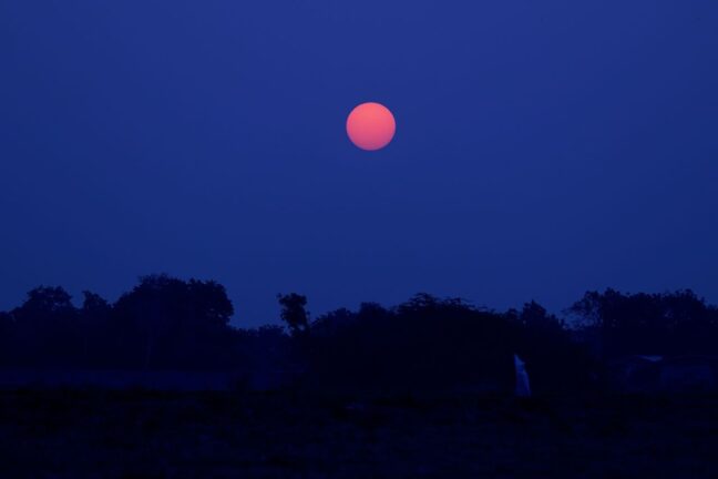 A captivating red moon shining brightly against a dark, silhouetted landscape during the night.