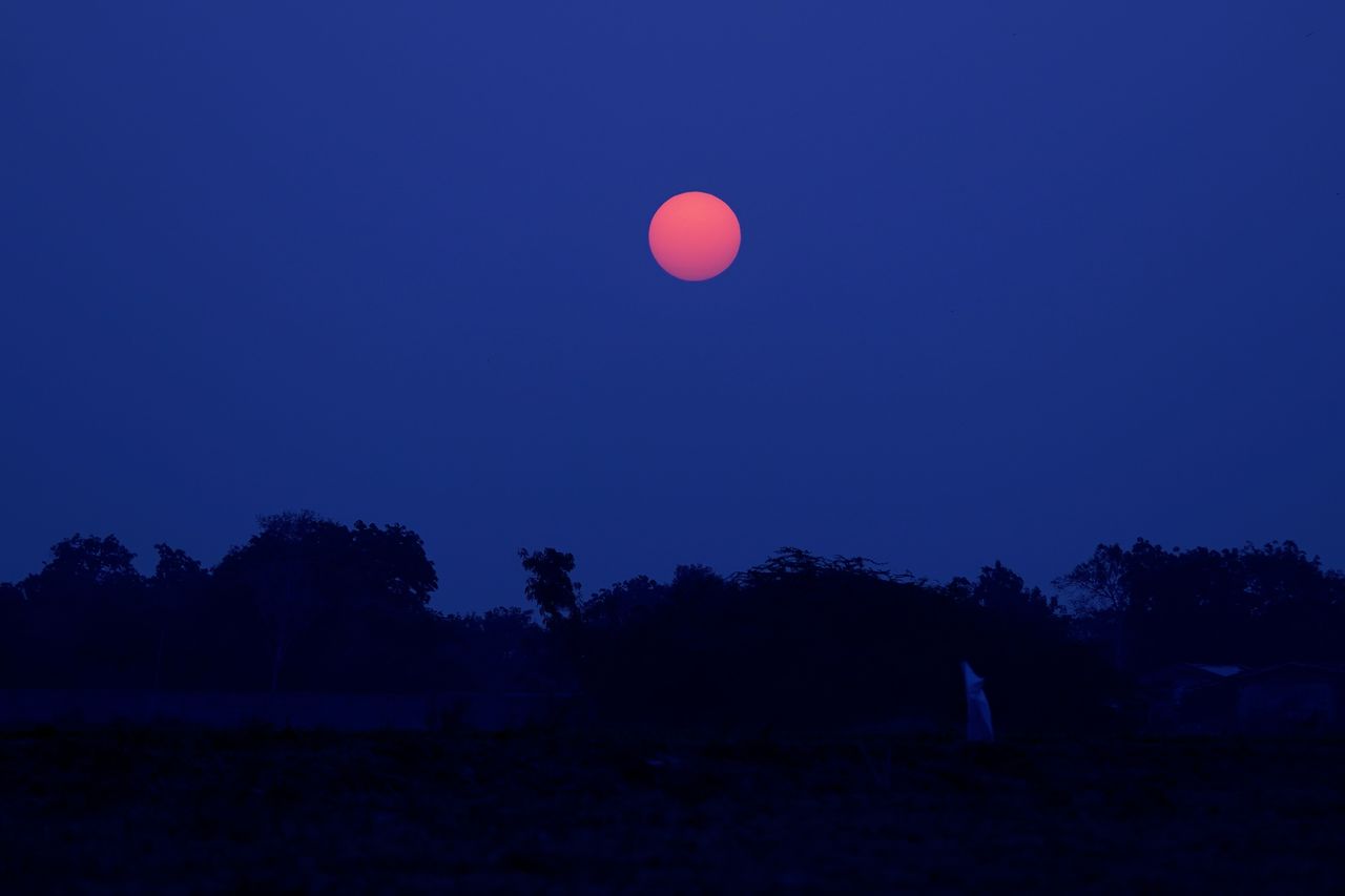 A captivating red moon shining brightly against a dark, silhouetted landscape during the night.
